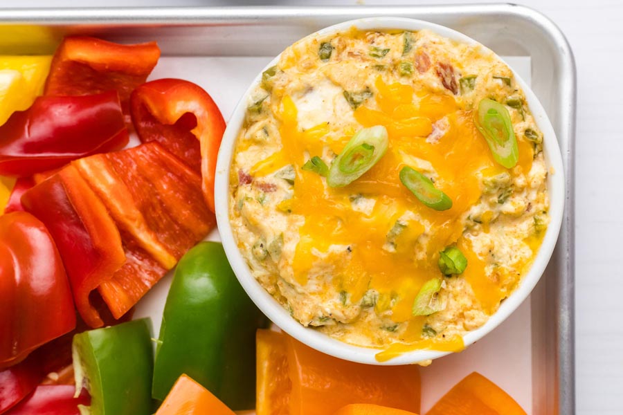 Creamy jalapeno popper dip topped with cheesy and green onion and sitting next to bell pepper slices.