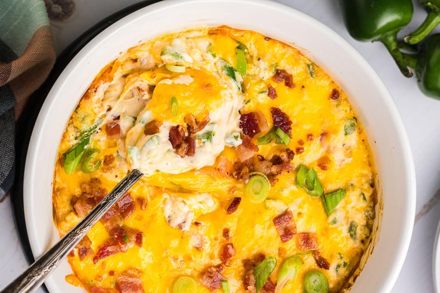 A spoon inside jalapeno popper dip topped with bacon.