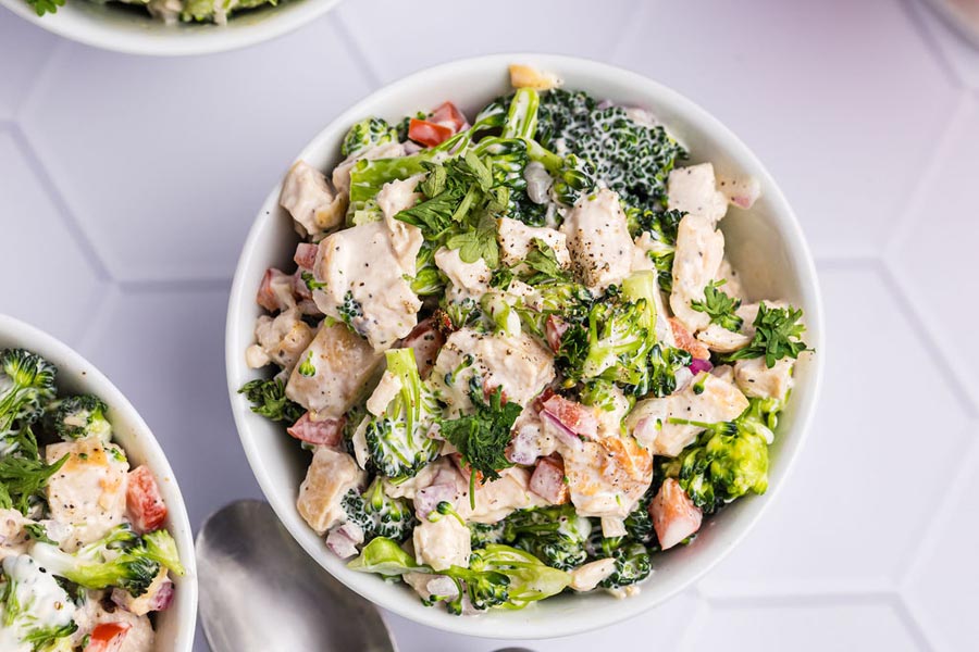 A bowl of creamy coated broccoli and chicken salad with bell pepper and onion.