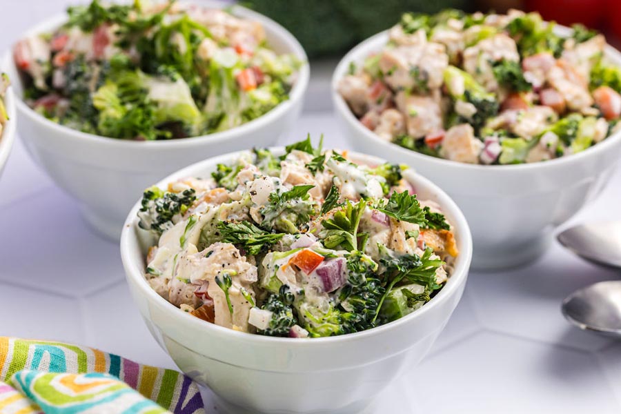 Three bowls of broccoli chicken salad topped with fresh parsley.