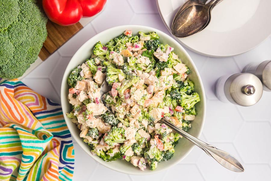 Looking down on a large bowl of chopped broccoli chicken salad with a serving spoon resting in the bowl.
