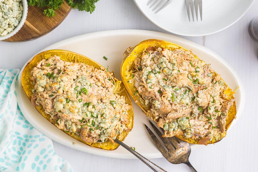 A plate of buffalo chicken stuffed in a spaghetti squash and topped with chives.