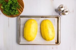 Two spaghetti squash halves on a parchment lined baking tray.