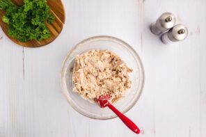 A glass bowl with buffalo chicken mixture and a red spatula.