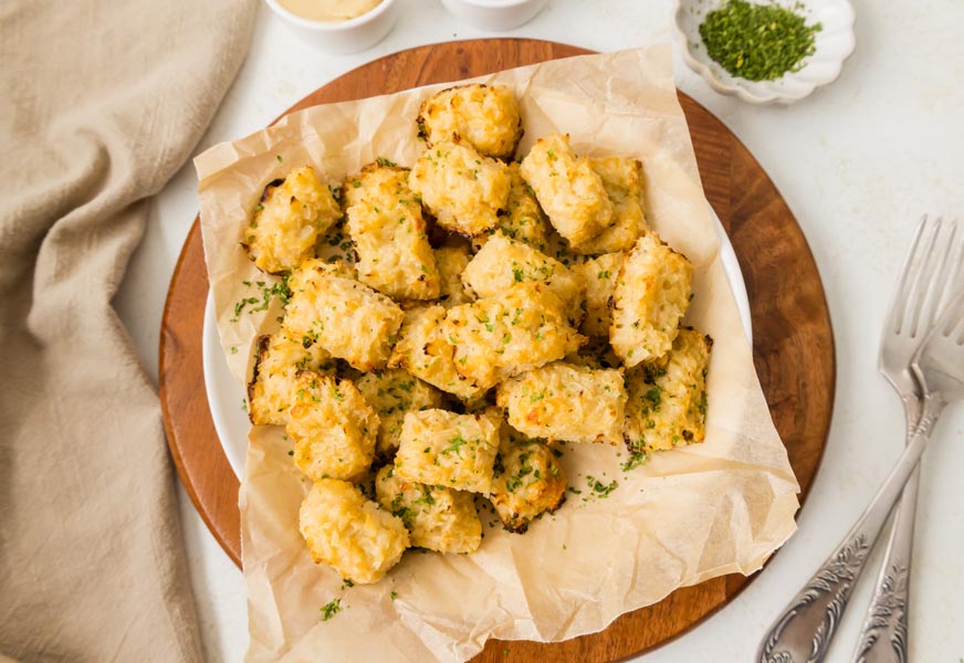 Cauliflower tater tots in a bowl next to chopped parsley and some forks.