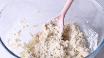 A pink spoon mixing a cauliflower rice with a creamy cheesy blend.