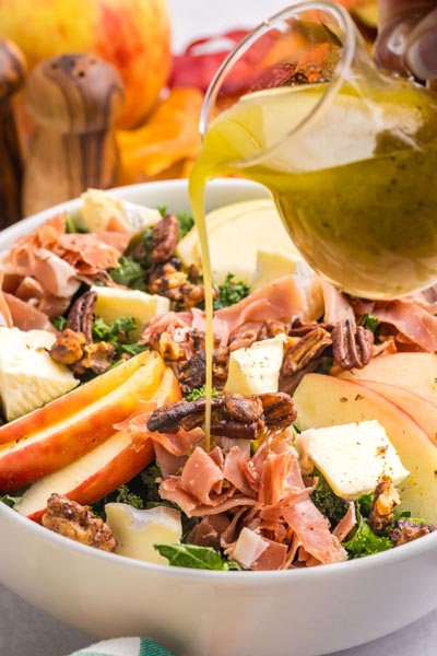 Pouring apple cider vinaigrette on a harvest salad.