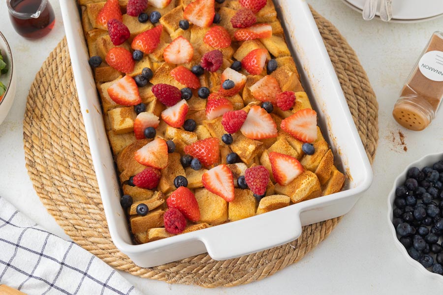 A white casserole dish filled with french toast casserole and topped with fresh berries.