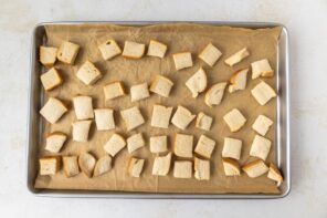 Bite sized chunks of keto bread spread on a parchment lined baking sheet.