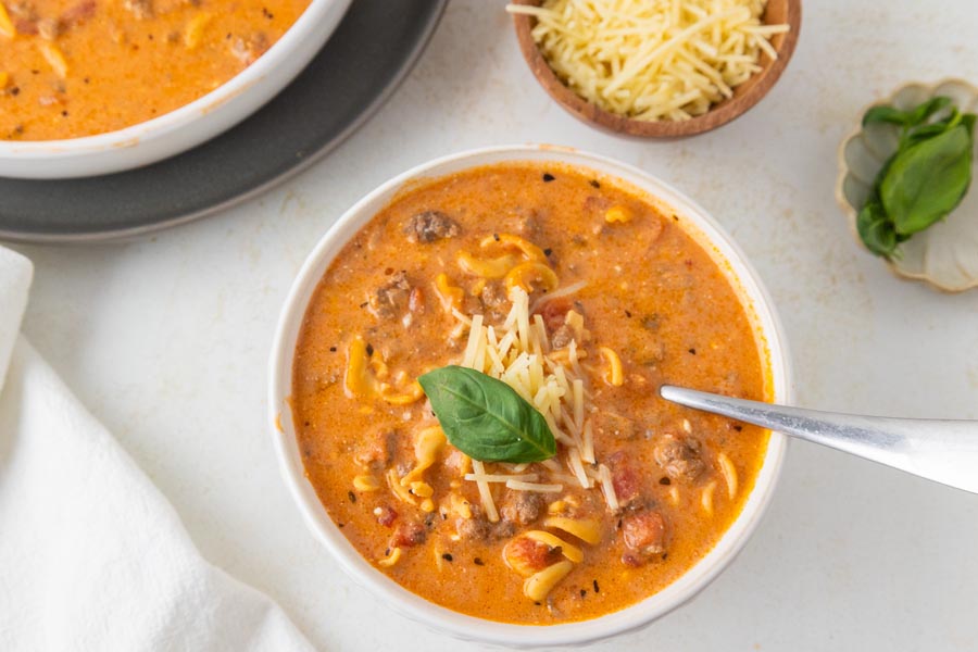 A spoon sitting in a bowl of creamy tomato soup topped with parmesan cheese and basil.