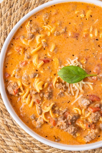 Close up of a bowl of tomato soup with spiral shaped pasta noodles.