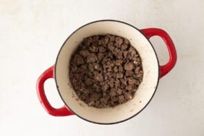 A dutch oven with cooked ground beef and onions.