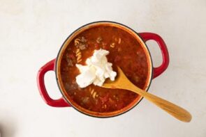 A big scoop of cream cheese sitting on top a pot of tomato soup waiting to be stirred in.