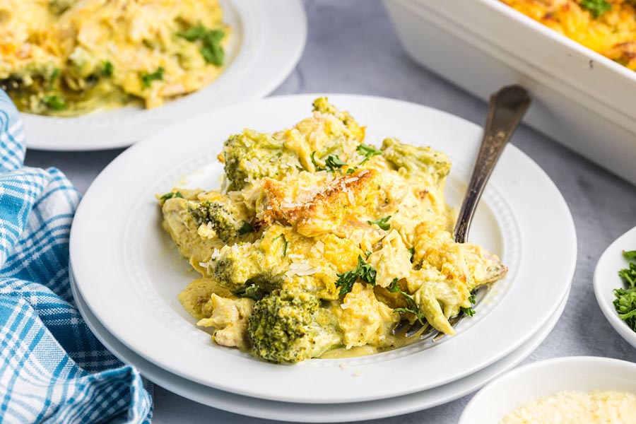 Cheesy chicken divan with chicken and broccoli on a white plate with a fork on the plate too.