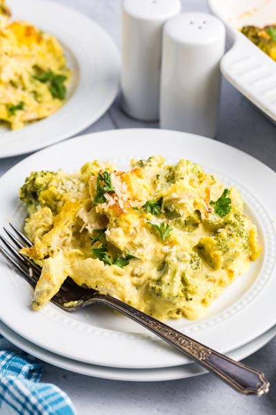 Chunks of broccoli and chicken smothered in a cream sauce on white plate with a fork.