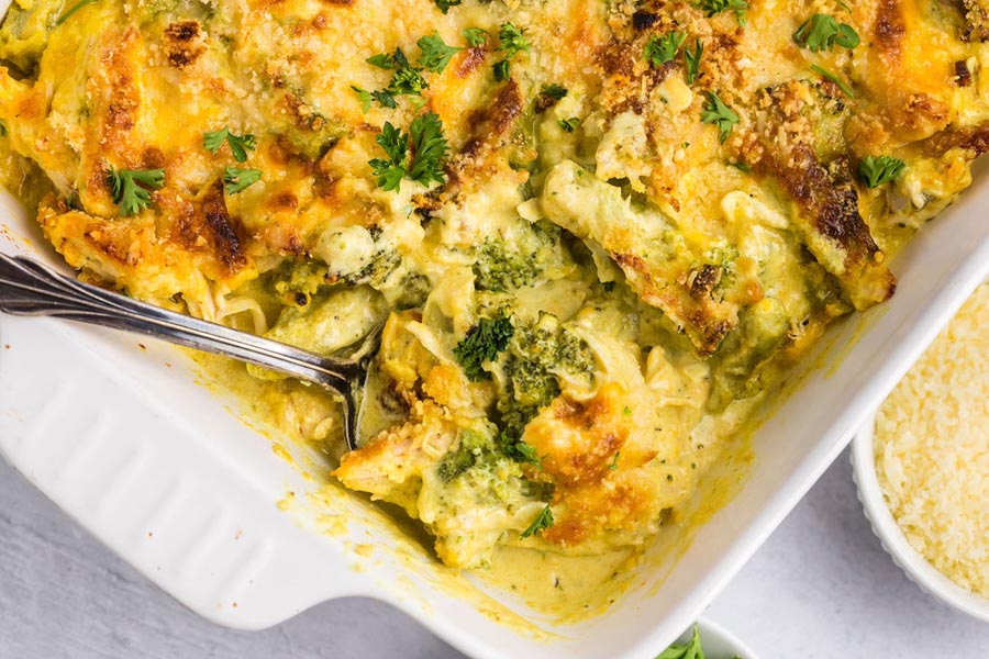 Chicken divan casserole in a white baking dish with a serving taken out and a spoon resting in the dish.