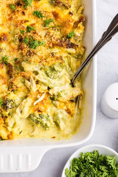 Creamy chicken casserole with cooked broccoli in a baking dish topped with parsley.