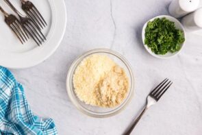 A mixture of almond flour and parmesan cheese in a small bowl next to a bowl of parsley and a fork.