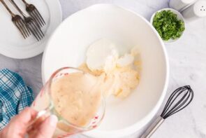 A hand pouring mushroom soup from a measuring cup into a large bowl.