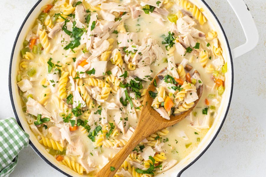 A wooden spoon holding a serving of chicken noodle casserole in a skillet.