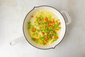 A white skillet with cooked vegetables - carrot, onion, celery in butter.