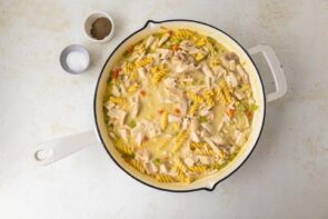 Chicken and noodles added to a casserole in a skillet.