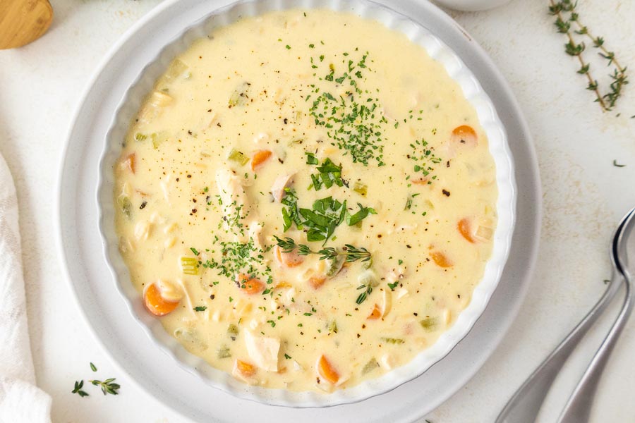 Looking down into a creamy soup filled with chicken, carrot and fresh herbs.