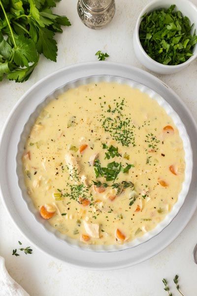 A bowl of chicken and rice soup topped with herbs and next to a bowl of fresh parsley.