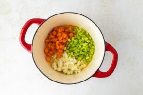 Sliced carrot, diced celery and onion in a red dutch oven.