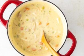 A wooden spoon stirring a pot of creamy chicken soup.