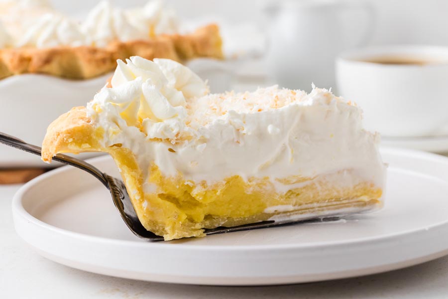 A slice of coconut cream pie placed on a white plate with a pie spatula.