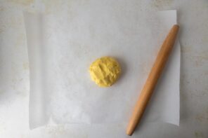 A ball of pie dough on a sheet of parchment paper next to a rolling pin.