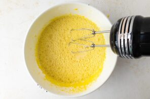 An electric mixer mixing a creamy egg yolk mixture.