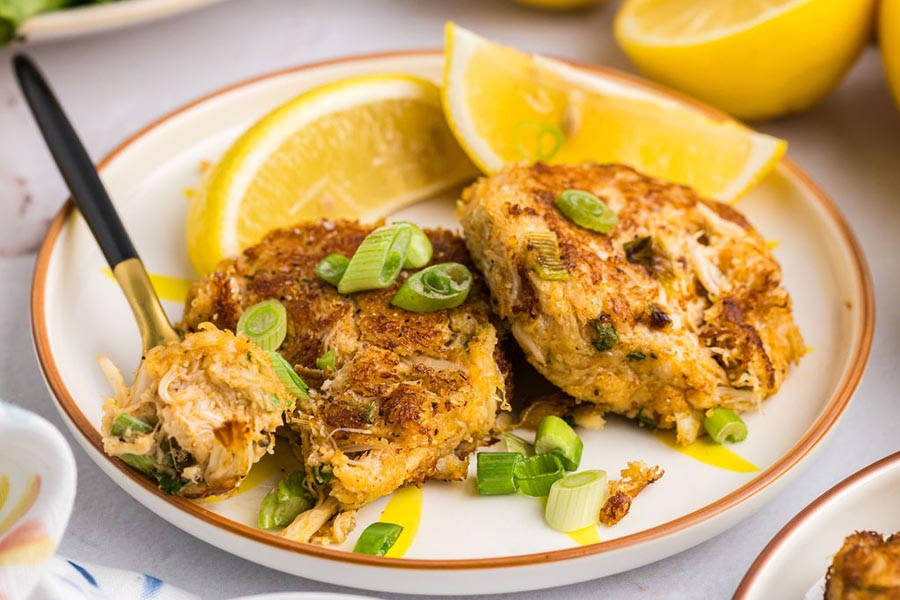 Two crab cakes on a plate with lemon slices.