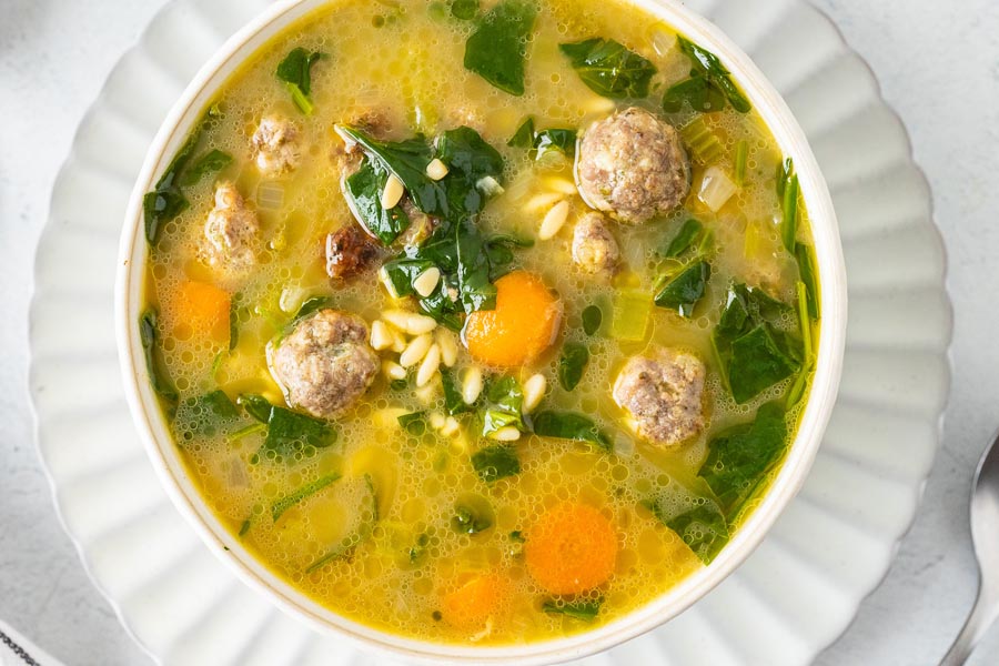 Looking down into a savory bowl of Italian wedding soup with meatballs and orzo pasta.