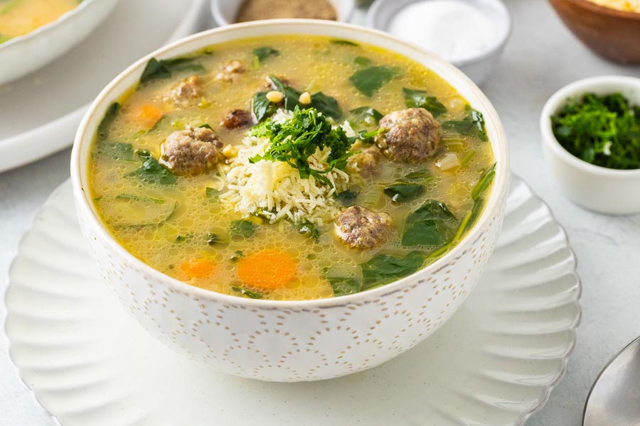 A bowl of meatball soup topped with parmesan cheese and parsely.