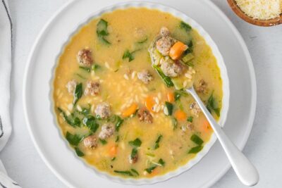 A spoon resting on a large bowl of Italian wedding soup.