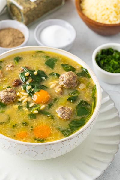 A bowl of meatball soup with spinach and carrot next to parsley and salt.