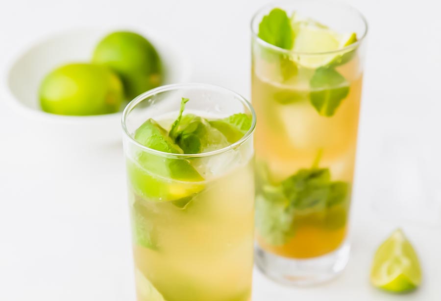 two cocktails filled with lime and mint with limes in the background