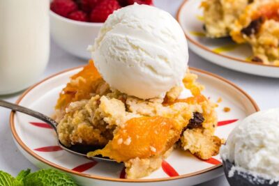 Warm, gooey peach cobbler on a plate topped with creamy ice cream.