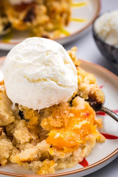 A scoop of vanilla ice cream on top of peach cobbler made with paula deen's recipe.