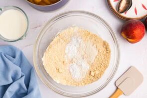 Dry ingredients in a mixing bowl next to a peach and a spatula.