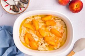 Sliced peaches and syrup on top of cobbler batter in a baking dish.