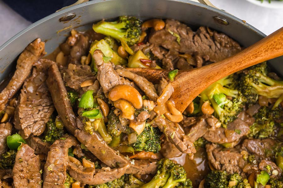 A skillet with cooked steak in a cashew broccoli sauce.