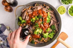 Pouring soy sauce into a skillet with beef, broccoli and sweet chili sauce.