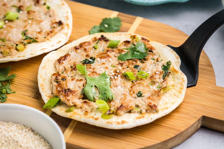 Grilled smashed taco filling with ground chicken and Asian spices on a wooden cutting board.