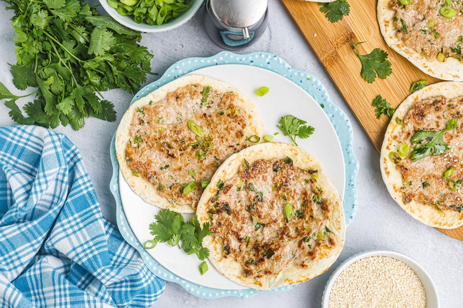 Two smashed dumpling tacos on a blue plate topped with green onion, cilantro and sesame seeds.