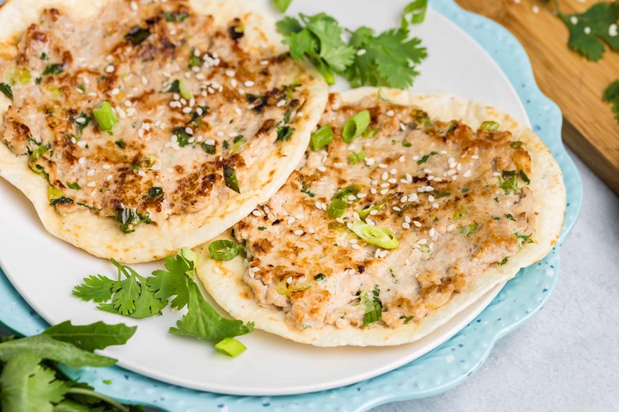 Fried smashed chicken tacos on a plate topped with cilantro, sesame seeds and green onion.