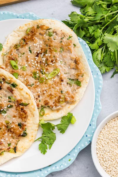 Dumpling chicken tacos stacked on a plate with cilantro and sesame seeds on the side.