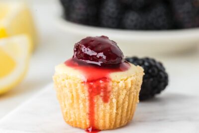 Close up of a single small mini cheesecake with graham cracker crust and topped with blackberry syrup.